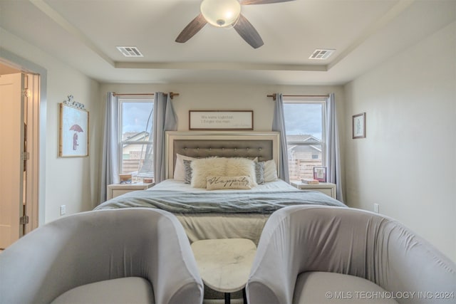 bedroom featuring multiple windows, a tray ceiling, and ceiling fan