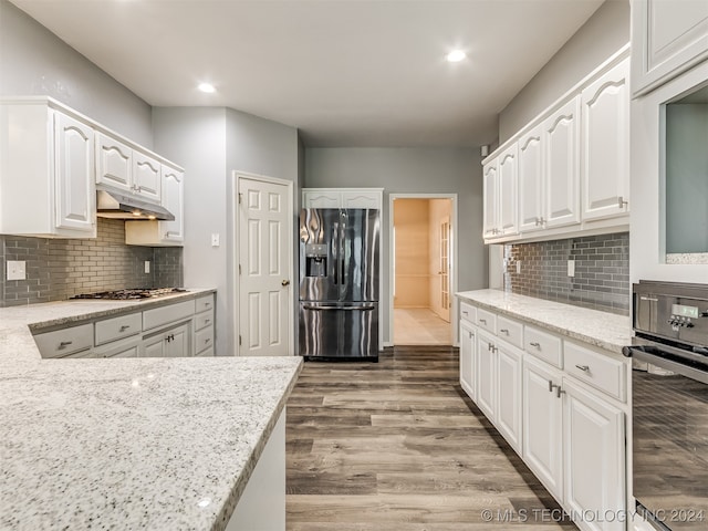 kitchen featuring hardwood / wood-style floors, light stone countertops, white cabinetry, and appliances with stainless steel finishes