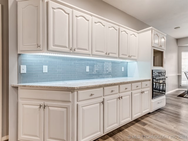 kitchen featuring tasteful backsplash, light stone counters, white cabinetry, light hardwood / wood-style flooring, and oven