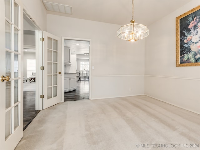 unfurnished room with french doors, carpet floors, and an inviting chandelier