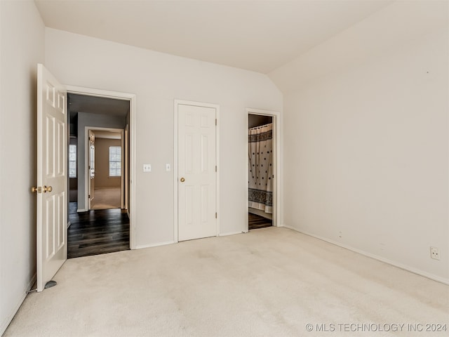 unfurnished bedroom with light hardwood / wood-style flooring, ensuite bath, and lofted ceiling