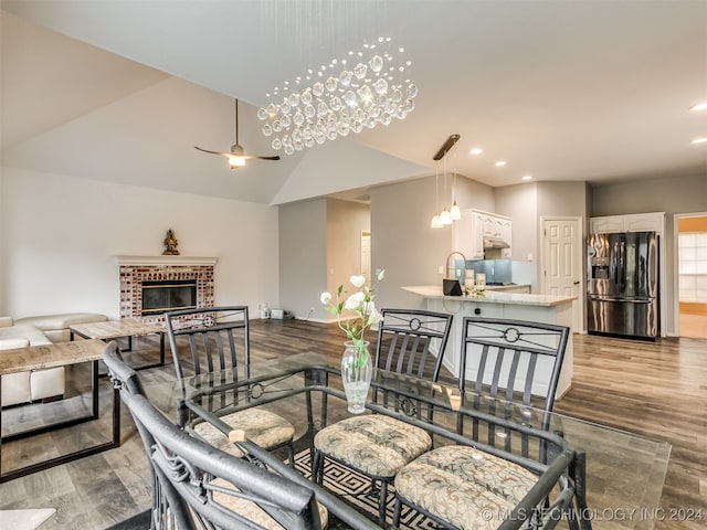 dining room with ceiling fan with notable chandelier, light hardwood / wood-style floors, a brick fireplace, and lofted ceiling