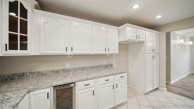 kitchen with light stone countertops, white cabinetry, light hardwood / wood-style floors, and beverage cooler