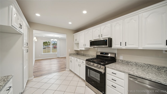 kitchen featuring white cabinetry, stainless steel appliances, light stone counters, light tile patterned floors, and a chandelier