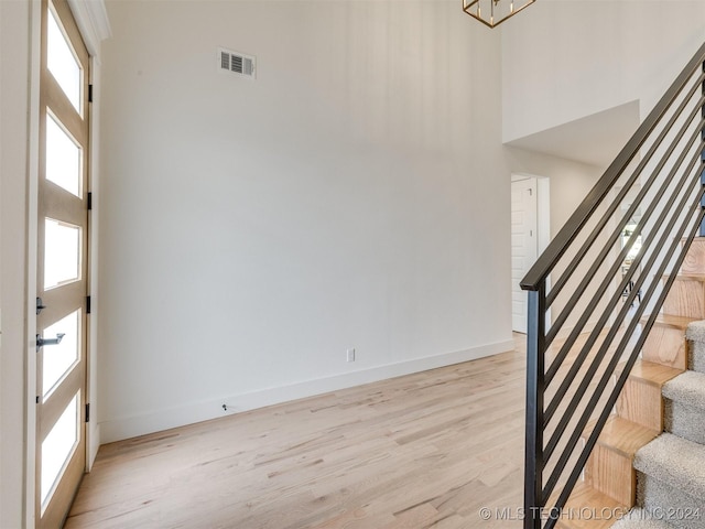 foyer entrance with visible vents, stairway, light wood-style flooring, a high ceiling, and baseboards