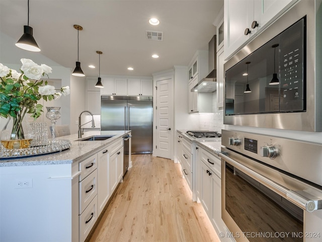 kitchen with built in appliances, a sink, visible vents, white cabinetry, and wall chimney range hood