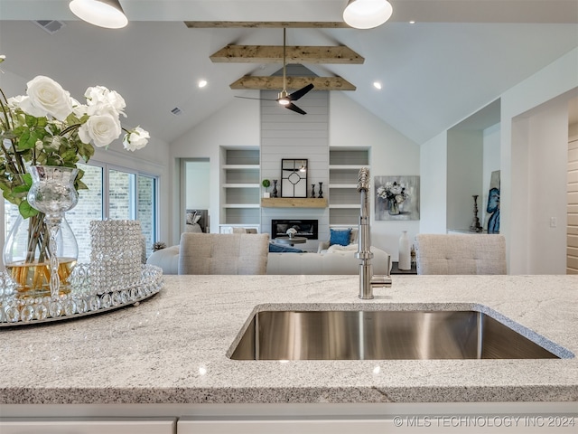 kitchen featuring beam ceiling, sink, light stone countertops, and a fireplace