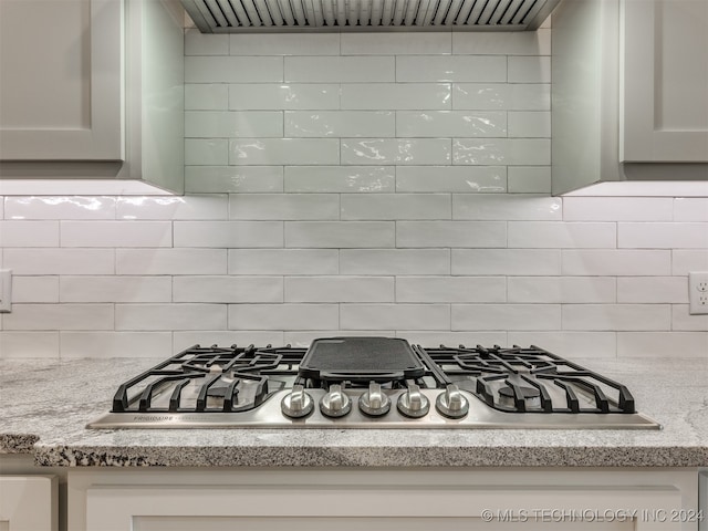 room details featuring stainless steel gas cooktop, decorative backsplash, light stone countertops, and exhaust hood