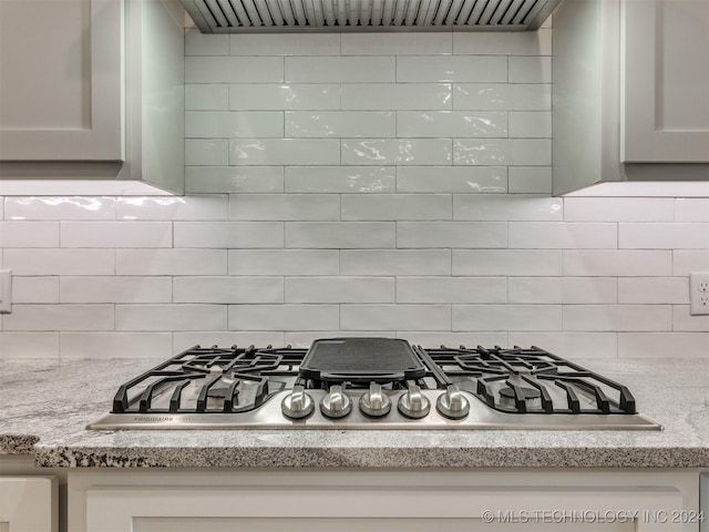 details featuring premium range hood, stainless steel gas cooktop, and decorative backsplash