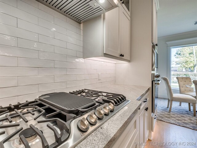 kitchen featuring appliances with stainless steel finishes, white cabinetry, light hardwood / wood-style floors, light stone counters, and ornamental molding