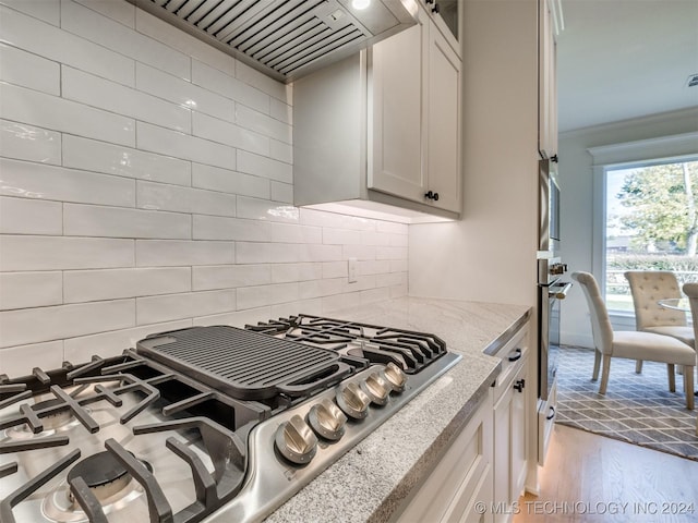 kitchen featuring appliances with stainless steel finishes, wood finished floors, light stone countertops, custom exhaust hood, and backsplash