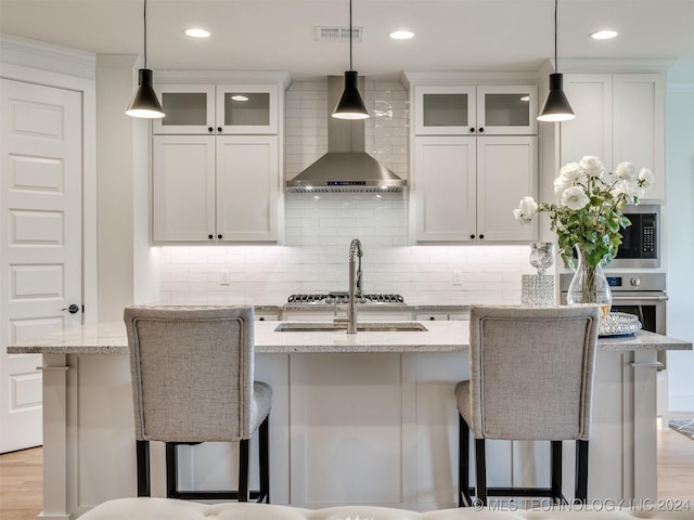 kitchen with a breakfast bar, visible vents, wall chimney range hood, decorative backsplash, and an island with sink