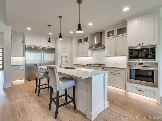 kitchen featuring built in appliances, wall chimney exhaust hood, a sink, and light wood-style flooring