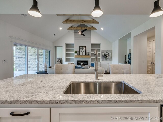 kitchen with vaulted ceiling with beams, sink, pendant lighting, light stone counters, and a fireplace