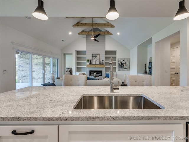 kitchen featuring open floor plan, a large fireplace, light stone counters, and hanging light fixtures