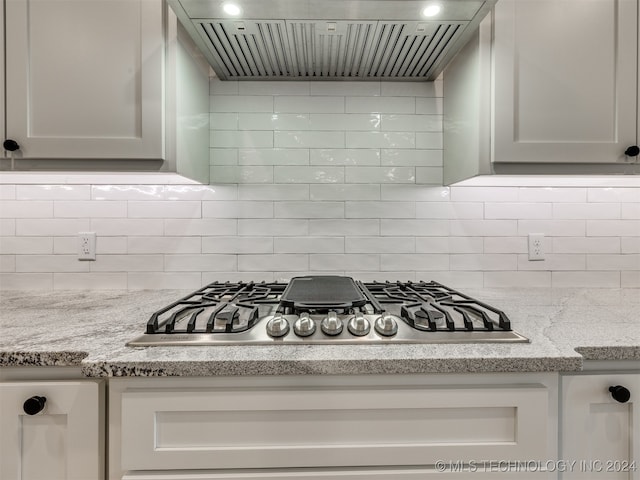 kitchen featuring wall chimney exhaust hood, stainless steel gas stovetop, white cabinets, light stone counters, and tasteful backsplash