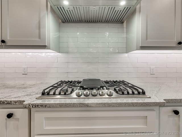 kitchen with wall chimney range hood, tasteful backsplash, stainless steel gas stovetop, and light stone counters