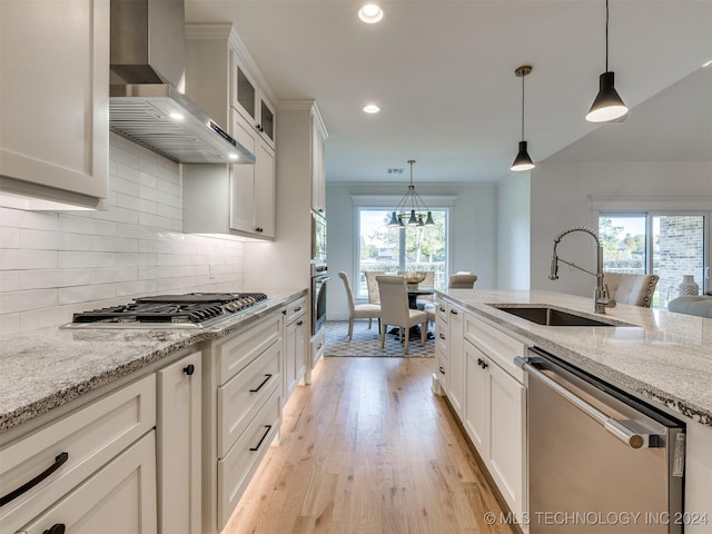 kitchen with wall chimney exhaust hood, appliances with stainless steel finishes, a sink, and a healthy amount of sunlight