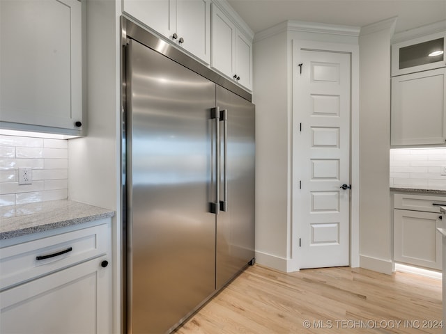 kitchen with built in fridge, light stone countertops, light wood-type flooring, white cabinets, and tasteful backsplash