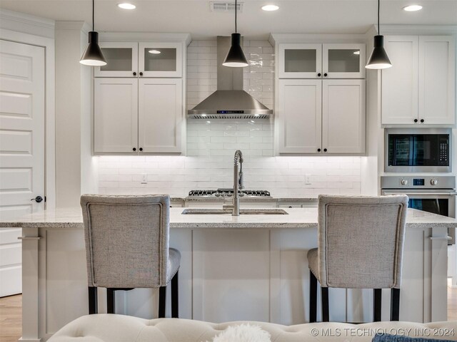 kitchen with white cabinetry, wall chimney exhaust hood, appliances with stainless steel finishes, and pendant lighting