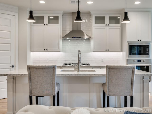 kitchen featuring a breakfast bar area, decorative backsplash, appliances with stainless steel finishes, wall chimney range hood, and an island with sink