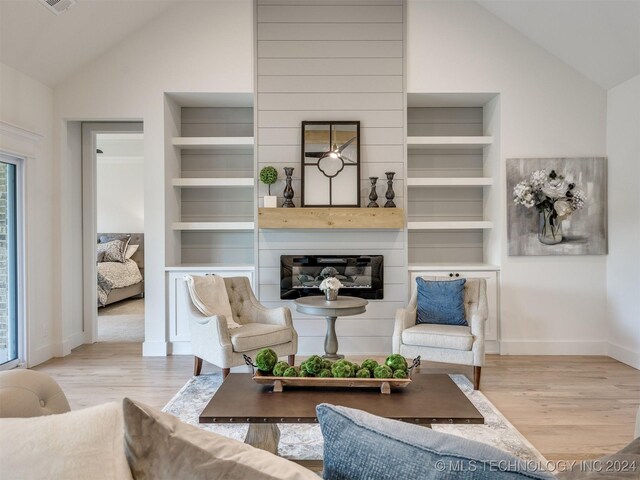 living room featuring light hardwood / wood-style flooring, high vaulted ceiling, a large fireplace, and built in shelves