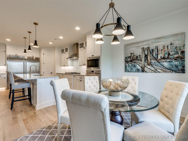 dining area with an inviting chandelier, ornamental molding, sink, and light hardwood / wood-style floors