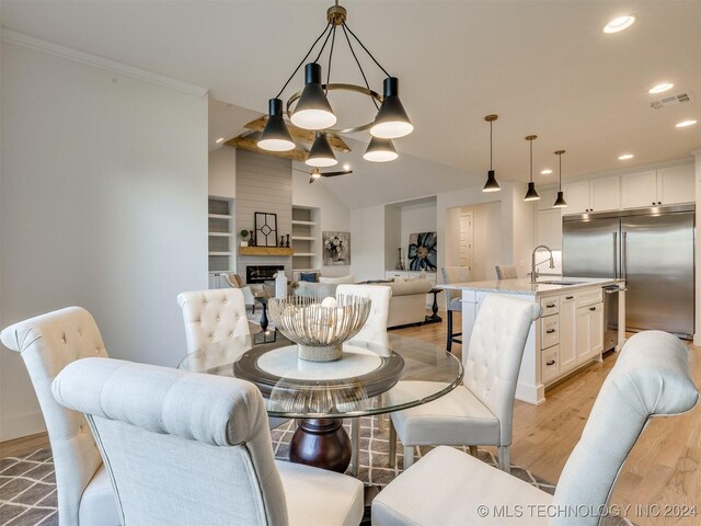 dining room featuring sink, vaulted ceiling, ornamental molding, light hardwood / wood-style flooring, and a chandelier