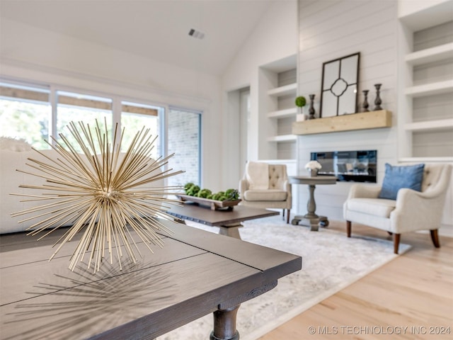 living area featuring built in shelves, a glass covered fireplace, a wealth of natural light, and wood finished floors