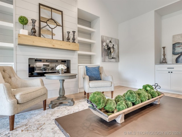 sitting room featuring built in features, lofted ceiling, a glass covered fireplace, wood finished floors, and baseboards