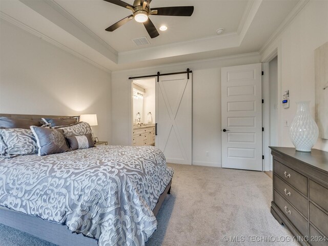 carpeted bedroom featuring ornamental molding, a barn door, a raised ceiling, ensuite bathroom, and ceiling fan