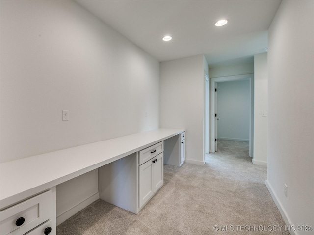 unfurnished office featuring recessed lighting, baseboards, built in desk, and light colored carpet