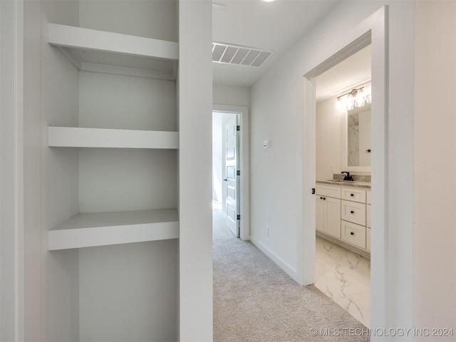 hallway featuring marble finish floor, visible vents, light carpet, a sink, and baseboards