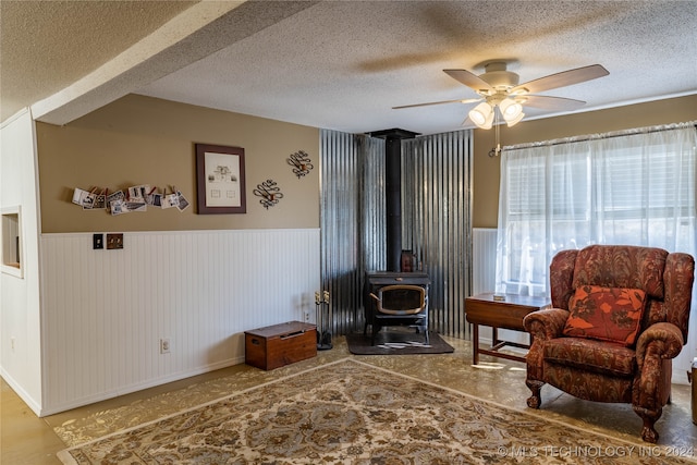 sitting room with ceiling fan, a wood stove, and a textured ceiling