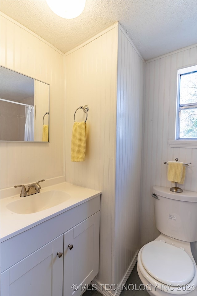 bathroom featuring vanity, a textured ceiling, toilet, and wood walls