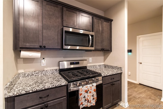 kitchen with light hardwood / wood-style flooring, light stone countertops, dark brown cabinets, and stainless steel appliances