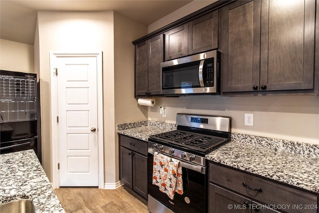 kitchen featuring dark brown cabinetry, appliances with stainless steel finishes, light stone countertops, and light hardwood / wood-style floors