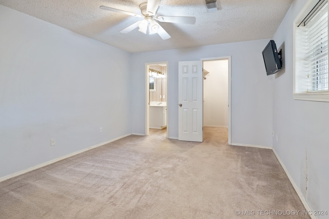 unfurnished bedroom featuring light carpet, ceiling fan, a textured ceiling, ensuite bathroom, and a walk in closet