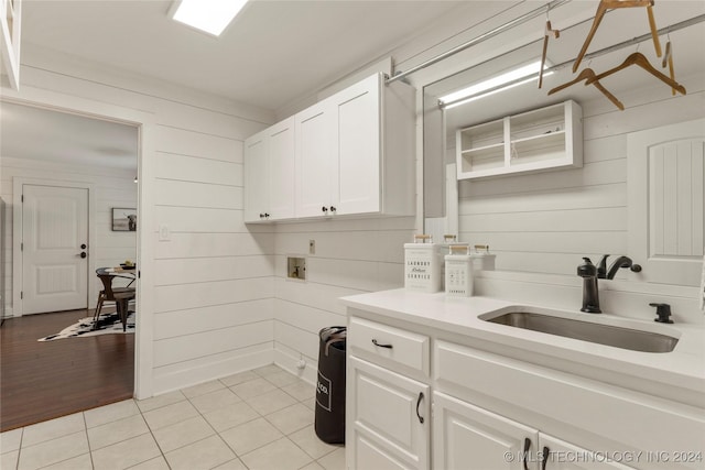 kitchen featuring light tile patterned flooring, white cabinetry, wooden walls, and sink