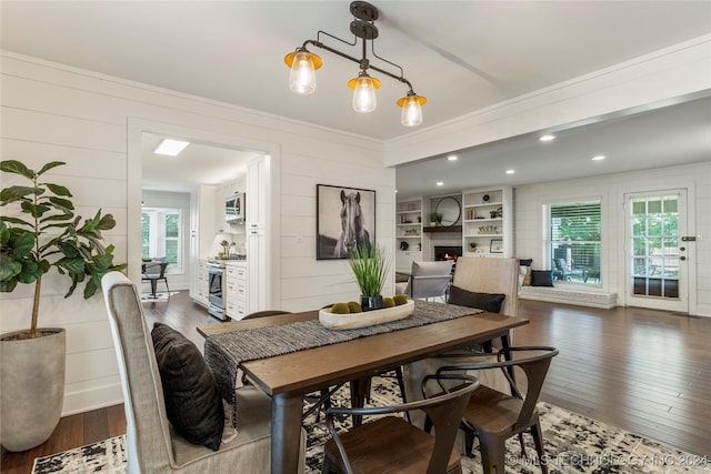 dining space featuring dark wood-type flooring, a healthy amount of sunlight, and wooden walls