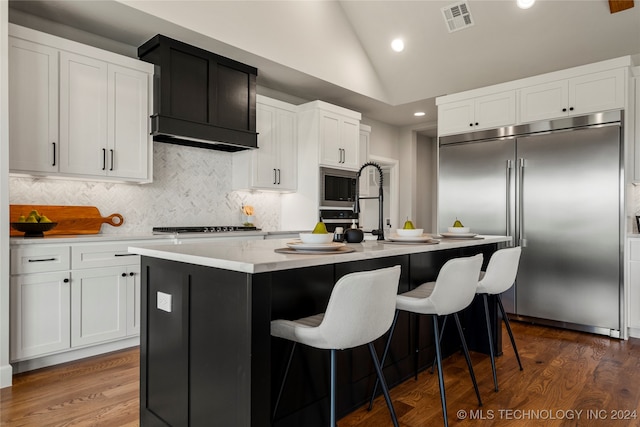 kitchen featuring lofted ceiling, a center island with sink, white cabinets, dark hardwood / wood-style floors, and appliances with stainless steel finishes