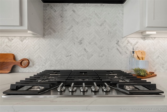 room details with white cabinetry, stainless steel gas cooktop, decorative backsplash, and light stone counters