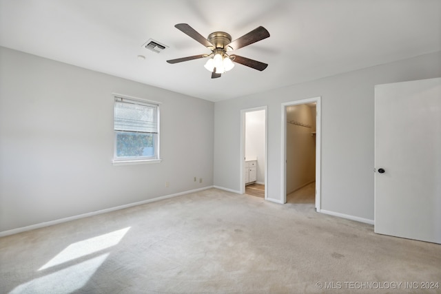 unfurnished bedroom featuring connected bathroom, a closet, a spacious closet, light colored carpet, and ceiling fan