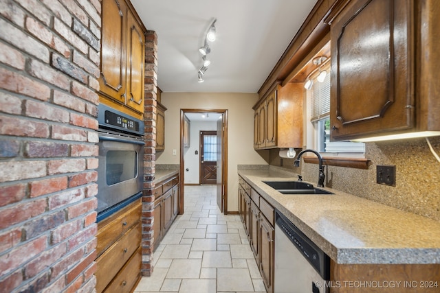 kitchen featuring tasteful backsplash, track lighting, sink, stainless steel appliances, and brick wall