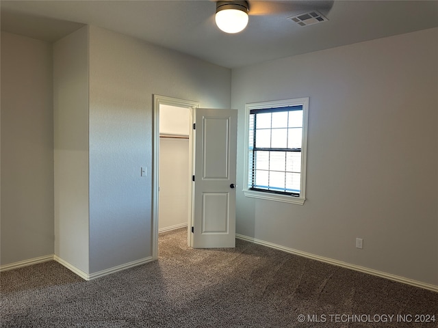 unfurnished bedroom featuring a spacious closet, a closet, ceiling fan, and dark colored carpet