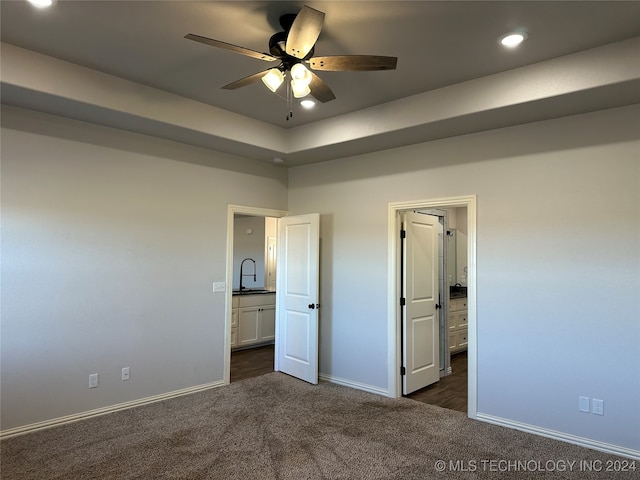 unfurnished bedroom featuring ceiling fan, ensuite bath, and dark carpet