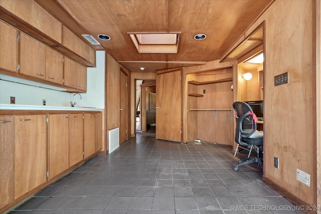 interior space with dark tile patterned flooring, wood walls, a skylight, sink, and wood ceiling