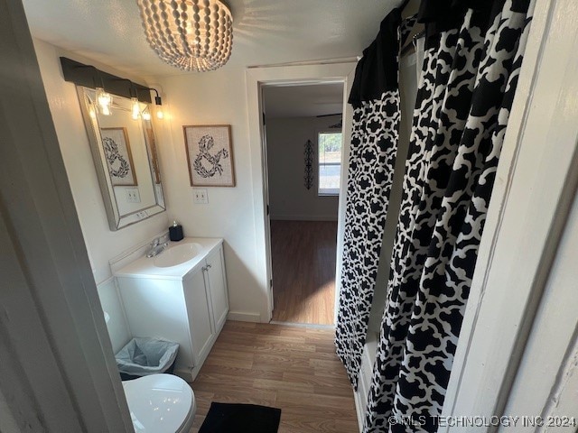 bathroom featuring wood-type flooring, toilet, a shower with curtain, vanity, and an inviting chandelier