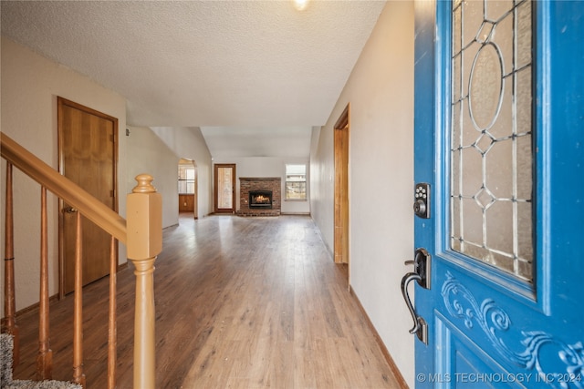 foyer with light hardwood / wood-style flooring, a textured ceiling, lofted ceiling, and a fireplace