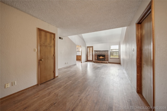 unfurnished living room featuring light hardwood / wood-style floors, a textured ceiling, vaulted ceiling, and a fireplace